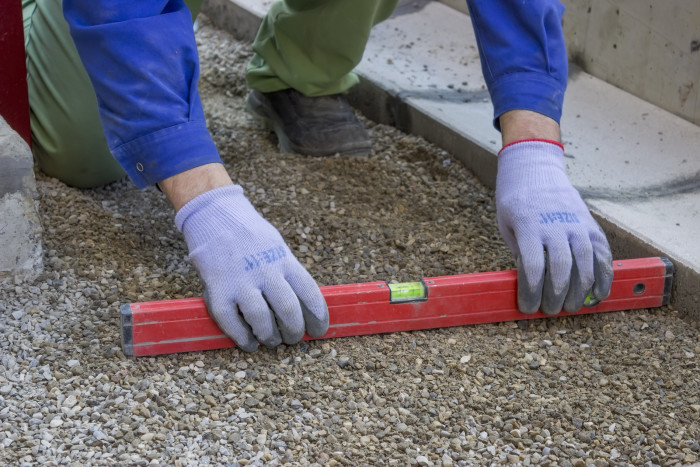 Worker checking horizontal level of ground for paving with leveling tool